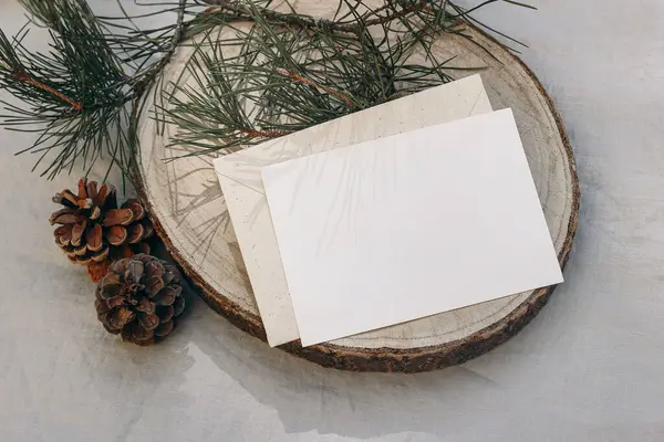 stock image Christmas stationery. Blank greeting card, invitation mockup on cut wooden round board. Green pine tree branch in sunlight. Grey linen tablecloth. Festive winter still life template, flat lay, top