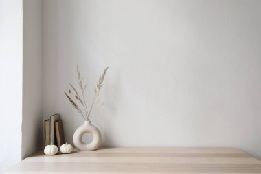Zarif huysuz İskandinav iç mimarisi. İçinde kuru ot buketi, eski kitaplar ve küçük beyaz balkabakları olan vazolar. Boş duvar arkaplanı. Modern oturma odası, ev ofisi, rahat bir dairede asgari sonbahar dekorasyonu..