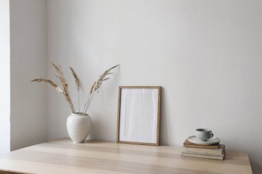 Sıcak İskandinav iç mimarisi. Kuru çim buketli vazo, eski kitaplar, bir fincan çay, kahve. Boş duvar arkaplanı. Modern oturma odası, ev ofisi. Yan görünüş, modern dairede en az sonbahar dekorasyonu..