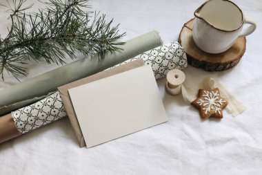 Noel hala hayattır. Tebrik kartı, davetiye modeli. Zencefilli kurabiye, beyaz keten masa örtüsünün üzerinde çam ağacı dalları. Yeşil desenli hediye paketi kağıtları. Süt sürahisi, kış kırtasiyesi.