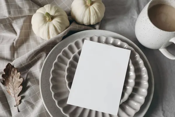 Neutral autumn stationery. Fall mockup scene with blank greeting card, invitation, craft envelope. White pumpkins. Scalloped plate, cup of coffee. Linen table cloth, oak leaves. Flatlay, Thanksgiving.