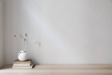 Elegant Scandinavian interior. White ball vase with dry grass, lagurus bouquet on old books. Empty wall background. Modern living room, home office, minimal moody autumn decor in cozy apartment. clipart