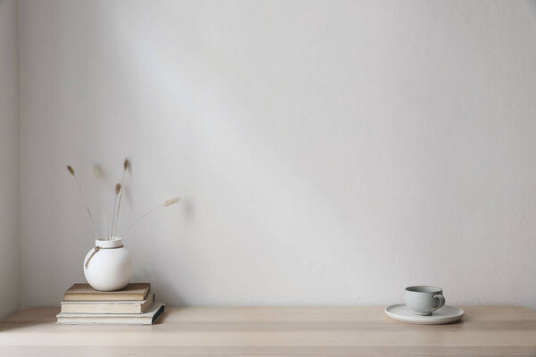 Modern interior. White vase with dray bunny tail grass. Cup of coffee and old books on wooden table. Empty beige wall background. Neutral mockup, scandinavian home, living room design.
