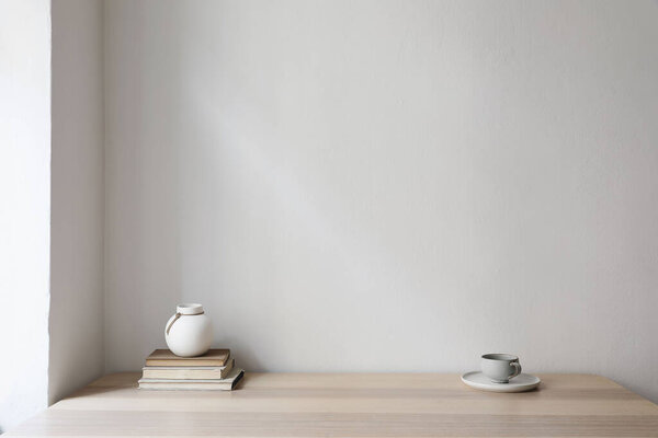 Modern interior, japandi home design. White vase, cup of coffee and old books on wooden table. Beige wall mockup background. Elegant living room, home office. No people, trendy indoor still life.
