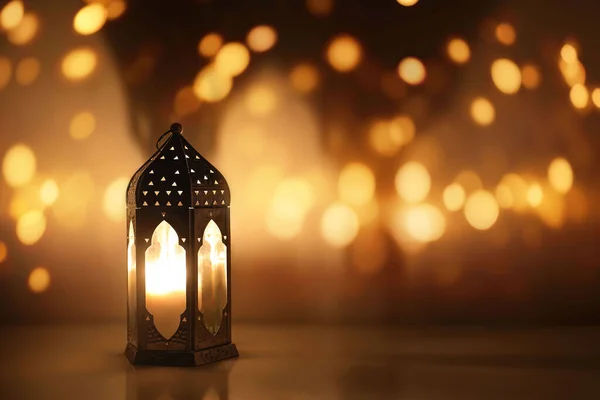 Dark silhouette of Moroccan lantern glowing at night. Glittering golden bokeh lights, blurred background. Ramadan Kareem, Eid ul Fitr muslim holiday still life, festive celebration concept.