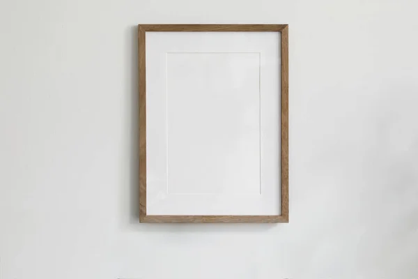 Single picture mockup poster hanging in middle of white wall. Portrait large 50x70, 20x28, a3,a4. Empty wooden frame mockup. Clean, modern, minimal design. Indoor interior decor, show text, or product
