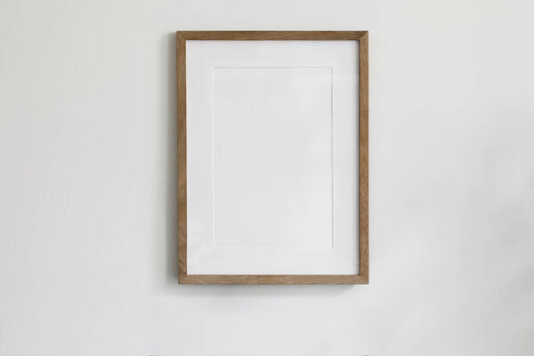 Single picture mockup poster hanging in middle of white wall. Portrait large 50x70, 20x28, a3,a4. Empty wooden frame mockup. Clean, modern, minimal design. Indoor interior decor, show text, or product