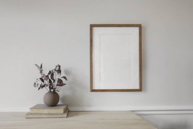 Boş dikey ahşap çerçeve ahşap masada taklit edilir. Kuru okaliptüs dalları olan modern bir vazo. Antika kitap yığını. Beyaz duvar arka planı, İskandinav ev iç mimarisi, dekor.
