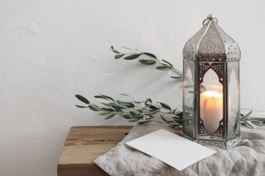 Ramazan Kareem tatili hala hayattadır. Zeytin dalları ile süslü Fas feneri. Boş tebrik kartı, ahşap masada davetiye modeli, bank, bulanık beyaz duvar arkaplanı.