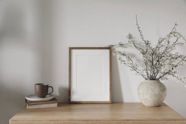 Bahar iç kısımları hala hayat. Bir fincan kahve, kitap yığınında çay. Bambu masasında seramik vazoda çiçek açan kiraz ağacı dalları. Dikey ahşap çerçeve, poster modeli, ev dekorasyonu.
