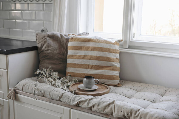 Капризный интерьер натюрморта. Чашка кофе, чай на деревянном подносе. Цветущие вишневые сливовые ветви. Сидя скамейка с постельными подушками под окном на кухне, пасхальный завтрак, домашний декор. Топ