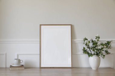 Bahar kahvaltısı hala hayattadır. Boş resim çerçevesi poster modeli. Çiçekli elma ağacı dalları olan beyaz seramik vazo. Bir fincan kahve, ahşap masada çay, eski kitaplarla dolu masa, Skandi 'nin iç mekanı.
