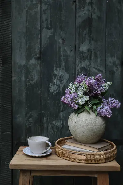 ムーディーファーム春の朝食はまだ生きています ホワイトライラックの花は コーヒー 紅茶のカップでテクスチャされた花瓶で花束を咲かせます ウィッカーのトレイ ヴィンテージの本 ぼやけた古い緑の木製のドアの背景 バーティカル — ストック写真