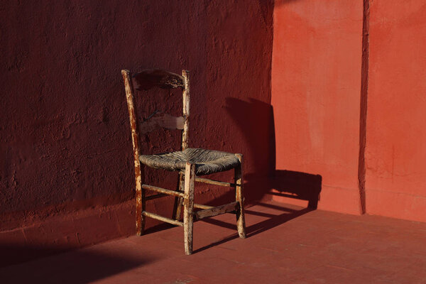 Old wooden one vintage chair in a room with red grunge walls and floor in sunlight, dark shadows. Shabby antique furniture. Empty copy space, no people., retro interior still life, concept.