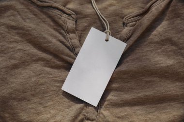 Katlanmış bej pamuklu tişörtte iple asılı fiyat etiketi. Giysi parçasının boş etiket modelinin kapanışı. Kıyafetler, moda ve alışveriş konsepti. Marka ekran, üst görünüm. Kimse yok..