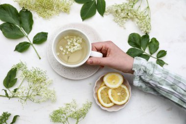 Çocuklar ellerinde bir fincan bitkisel elder çiçeği çayı tutuyorlar. Kareli gömlek. Bulanık oak ahşap masa arka planı. Elder çiçekleri, yapraklar ve taze limon dilimleri. Sağlıklı bir yaşam tarzı. Sambucus niger, üst görünüm