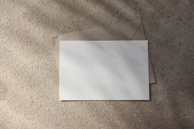 Boş yatay tebrik kartı davetiyesi maketi, el işi zarf. Güneş ışığında bej kireçtaşı arka planı. Palmiye yaprağı gölgesi. Modern marka şablonu. Tropik yaz, tatil, düz yatak, üst