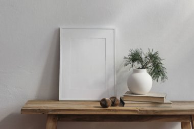 Noel Skandalı iç dekorasyon. Dikey beyaz çerçeve modeli. Klasik ahşap bank, masa. Çam ağacı dalları olan modern bir vazo. Eski kitaplardaki kağıt noel baloları, beyaz duvar arkaplanı..
