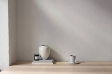 Zarif İskandinavya iç tasarımı. Ahşap masa, bir yığın dergi, kitaplar. Beyaz vazo, mum. Bir fincan kahve, çay. Boş beyaz duvar arka plan modeli. Güzel oturma odası hala hayat dolu. Ev dekoru.