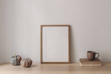 Sonbahar iç kısımları hala hayat dolu. Boş ahşap fotoğraf çerçevesi, balkabaklarıyla birlikte masanın üzerinde. Şükran Günü, Cadılar Bayramı ev dekorasyonu. Scandi 'nin içi. Bir fincan çay, kitaplarda kahve, beyaz duvar arkaplanı.