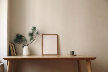 Zarif bir Noel tasarımı. Kış evi hala hayat. İskandinav dekoru. Boş dikey resim çerçevesi modeli, bir fincan kahve çayı. Tahta masa, masa. Çam ağacı dalları, vazo, bej duvar arkaplanı