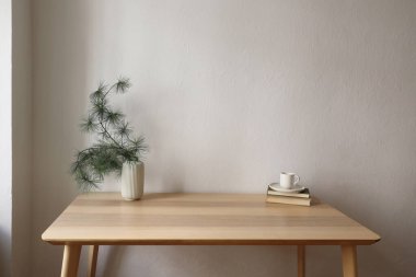 Zarif bir Noel Scandi iç mekanı. Ahşap masa. Çam ağacı dalları olan bir vazo, eski kitapların üzerinde bir fincan kahve. Beyaz duvar arka plan modeli. Minimum şenlikli ev dekorasyonu. İnsan yok. Boş kopyalama alanı.