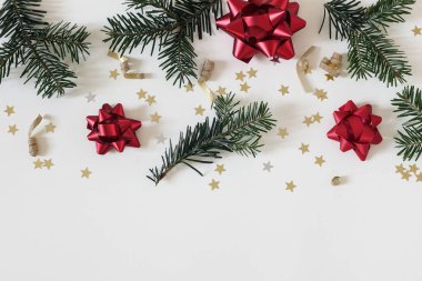 Noel kompozisyonu. Firavun ağacı dalları, altın yıldız konfetileri, kırmızı metalik hediye yayları beyaz masa arkasında izole edilmiş kurdeleler. Noel yatağı, dekoratif desen. Kış web pankartı, üst görünüm.