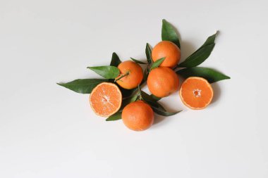 Dekoratif taze meyve kompozisyonu. Tam ve dilimlenmiş portakal mandalinası, narenciye ve beyaz masa arkasında izole edilmiş yapraklar. Yemek deseni. Boşluk. Düz konum, üst manzara, Akdeniz tasarımı.