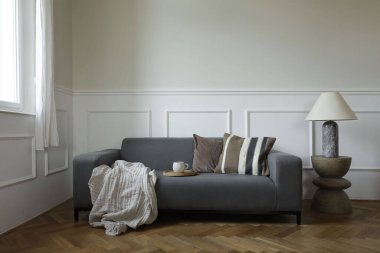 Sıcak İskandinav oturma odası. Pencerenin yanında kahverengi yastıklı gri kanepe. Modern boho ahşap sehpa, mermer lamba. Meşe parke döşeme. Bir fincan çay, kahve, zarif nötr ev dekorasyonu..