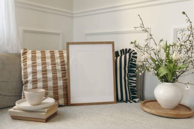 Bahar İskandinav oturma odasının iç kısmı. Ahşap çerçeve, poster modeli. Kanepe, keten çizgili, kareli yastıklar, bir fincan kahve. Kiraz çiçekleri, vazoda laleler, zarif ev dekorasyonu..