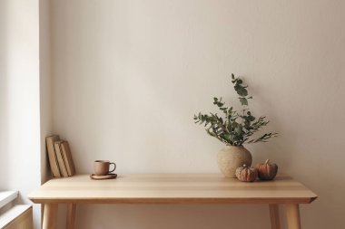 Sonbahar iç kısımları hala hayat dolu. Okaliptüslü vazo, zeytin dalı, balkabağı. Bir fincan çay, kahve, kitaplar. Penceredeki tahta masa. Merkez ofis. Minimal Scandi iç mimarisi, boş beyaz duvar arkaplanı.