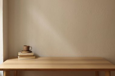 Minimalist zarif iç mekan. Ahşap masa, eski kitaplar seramik kahve, çay fincanı. Yumuşak doğal ışık, düz bej duvar arkaplanı. Sakin ve rahat bir atmosfer. Boş kopya alanı, kahvaltı konsepti