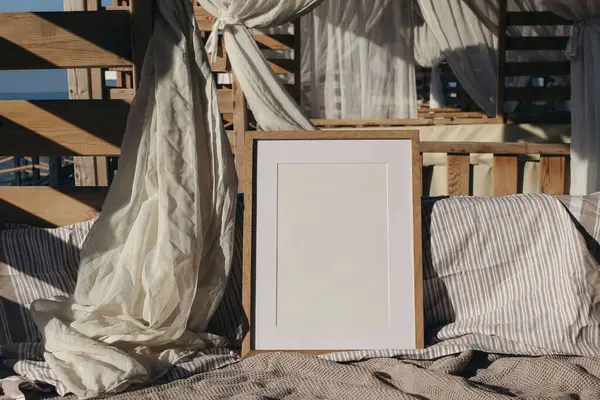 Boş ahşap çerçeve modeli. Çizgili ve dokulu çarşafları olan rahat bir açık hava yatağı. Yumuşak beyaz perdeler, ılık güneş ışığında doğal ahşap elementler, yaz tatili kabini titreşimleri..