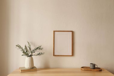 Akdeniz oturma odasının içi. Bir fincan kahve çayı, masada eski kitaplar. Beyaz duvar arka planı. Beyaz duvarda asılı boş ahşap çerçeve modeli. Zeytin dallı vazo.