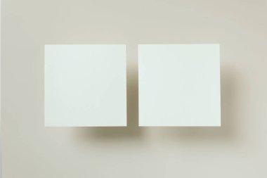 İki beyaz kare tebrik kartının minimalist kompozisyonu, açık bej arka planda gölgeler bırakan davetiye modelleri. Zarif markalaşma şablonları. Modern temiz görsel, düz yatış, üst görünüm.