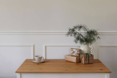 Elegant Christmas table still life. Vase with pine tree branches, gift boxes with ribbons. Cup of coffee, tea. Minimal natural home decoration. Scandinavian style winter decor, festive interior.