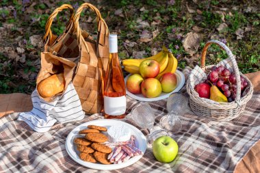 Dokuma sepetleri, taze meyveler, ekmek, şarap ve battaniyelerin olduğu davetkar bir piknik seti. Doğada sakin bir günün tadını çıkaran arkadaşlar, aileler ve çiftler için mükemmel bir ortam.