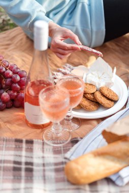 Doğal bir ortamda bir bardak gül şarabı, taze kırmızı üzüm, peynir ve kurabiyelerin bulunduğu rahat bir piknik düzeni, rahatlatıcı bir atmosfer yaratıyor. Piknik zamanı, bahar ayarı..