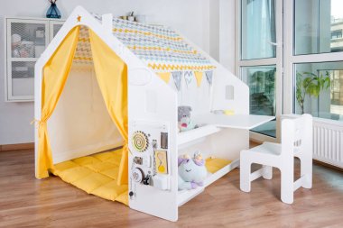 Etkileşimli oyuncaklar, modern tasarım mobilyaları ve eğlence ve yaratıcılık için parlak ve neşeli bir yaşam alanına yerleştirilmiş küçük bir masa içeren büyüleyici bir çocuk oyun çadırı. Modern çocuklar oyun alanı.
