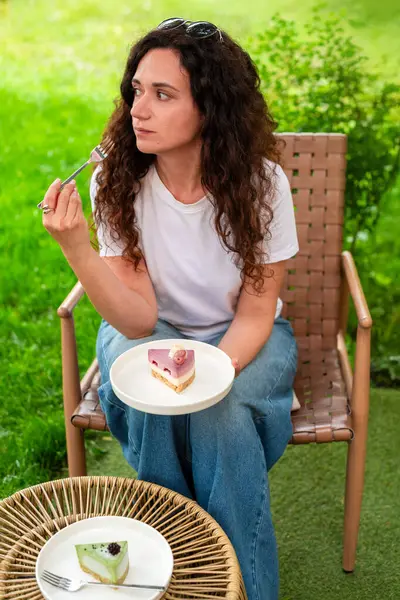 İki tabak tatlısıyla açık bir masada oturan bir kadın, huzurlu yeşil bir bahçede manzaranın ve sakin çevrenin tadını çıkarıyor. diyet konsepti, perhiz, diyet, kilo verme, diyet yapan kadın.