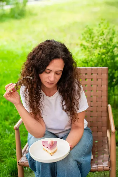 İki tabak tatlısıyla açık bir masada oturan bir kadın, huzurlu yeşil bir bahçede manzaranın ve sakin çevrenin tadını çıkarıyor. diyet konsepti, perhiz, diyet, kilo verme, diyet yapan kadın.