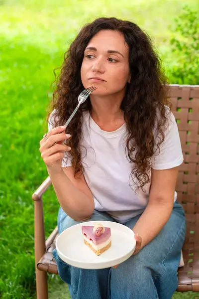 İki tabak tatlısıyla açık bir masada oturan bir kadın, huzurlu yeşil bir bahçede manzaranın ve sakin çevrenin tadını çıkarıyor. diyet konsepti, perhiz, diyet, kilo verme, diyet yapan kadın.