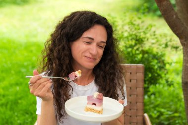 Genç bir kadın dışarıda oturmuş doğa ve huzur dolu yeşilliklerle çevrili lezzetli bir tatlıyı yiyor. Ayarlar rahatlamayı, tatlı anların tadını çıkarmayı ve doğayla bağlantıyı yansıtıyor.