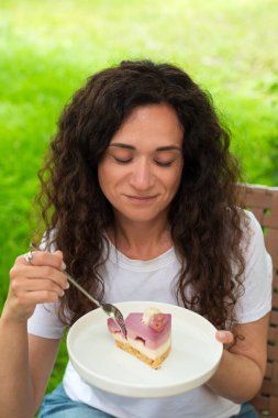 Genç bir kadın dışarıda oturmuş doğa ve huzur dolu yeşilliklerle çevrili lezzetli bir tatlıyı yiyor. Ayarlar rahatlamayı, tatlı anların tadını çıkarmayı ve doğayla bağlantıyı yansıtıyor.