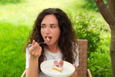 Genç bir kadın dışarıda oturmuş doğa ve huzur dolu yeşilliklerle çevrili lezzetli bir tatlıyı yiyor. Ayarlar rahatlamayı, tatlı anların tadını çıkarmayı ve doğayla bağlantıyı yansıtıyor.