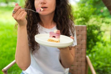 Genç bir kadın dışarıda oturmuş doğa ve huzur dolu yeşilliklerle çevrili lezzetli bir tatlıyı yiyor. Ayarlar rahatlamayı, tatlı anların tadını çıkarmayı ve doğayla bağlantıyı yansıtıyor.