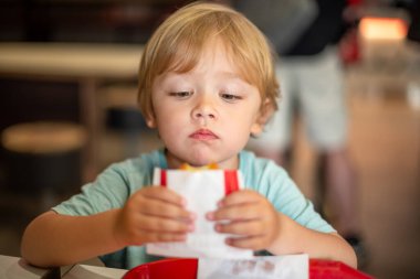 Günlük yemek ortamında fast food yemekten hoşlanan küçük bir çocuk. Dört yaşındaki bir çocuk restoranda mutlu bir şekilde yemek yiyor. Çocuk diyeti, kötü yemek seçenekleri, erken dönem abur cubur bağımlılığı..