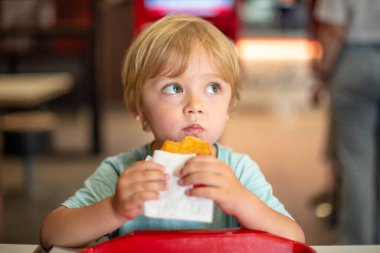 Günlük yemek ortamında fast food yemekten hoşlanan küçük bir çocuk. Dört yaşındaki bir çocuk restoranda mutlu bir şekilde yemek yiyor. Çocuk diyeti, kötü yemek seçenekleri, erken dönem abur cubur bağımlılığı..