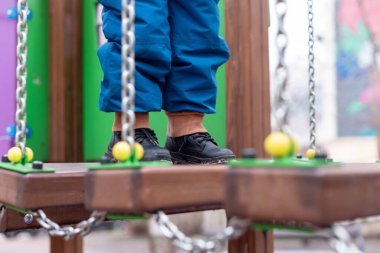 Zincirler ve renkli ahşap elementlerle çocuk parktaki köprüde yürüyor