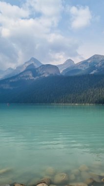 Louise Gölü, Alberta, Kanada - 8 Ağustos 2023: Louise Gölü 'nde turkuaz suda yüzen kırmızı kano. Güneşin doğuşunda Louise Gölü 'nde kano yapan çift.